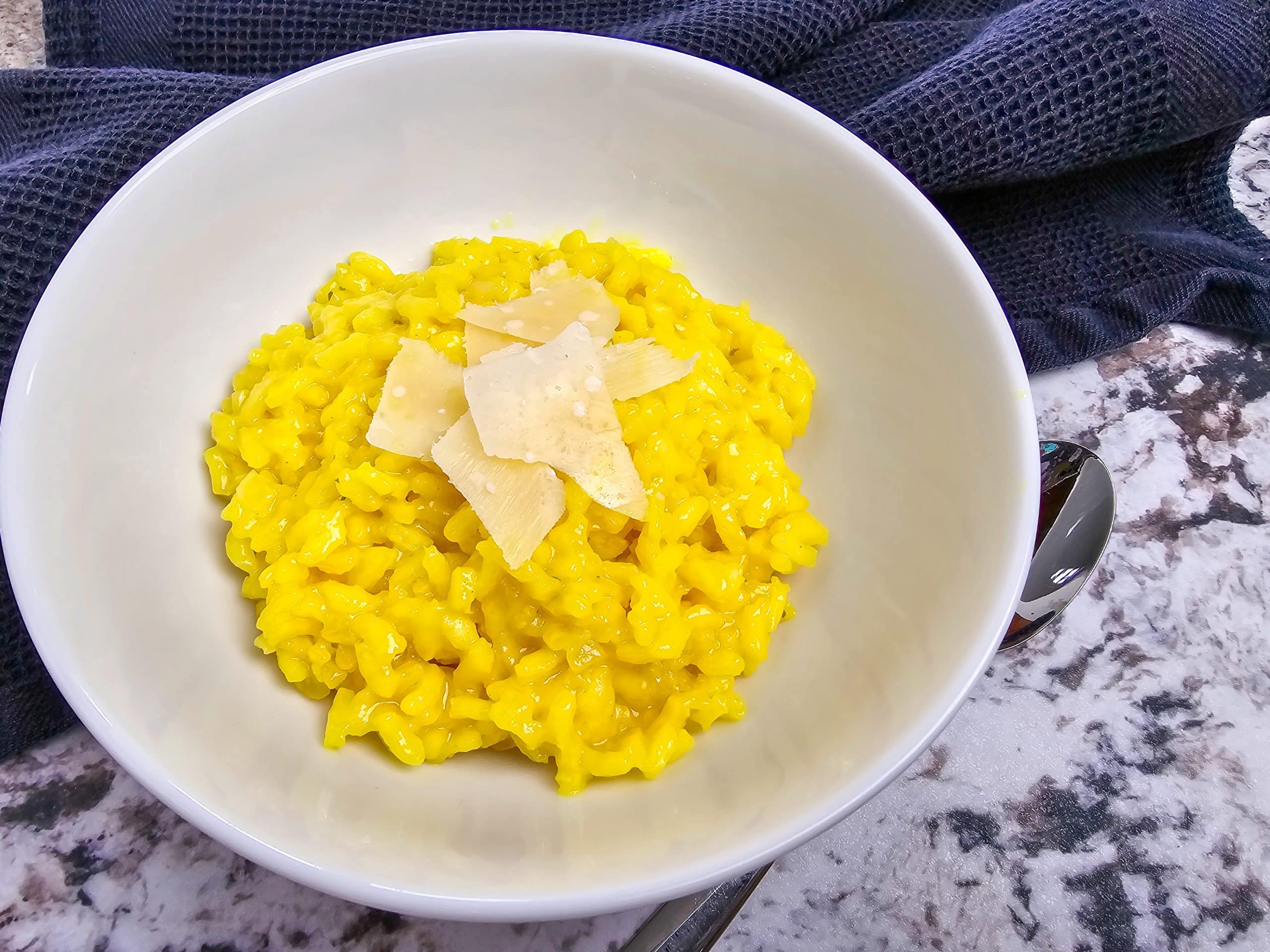 saffron risotto with Parmesan shavings in a white bowl on a granite countertop